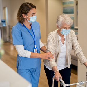 nurse is helping a senior walk post surgery